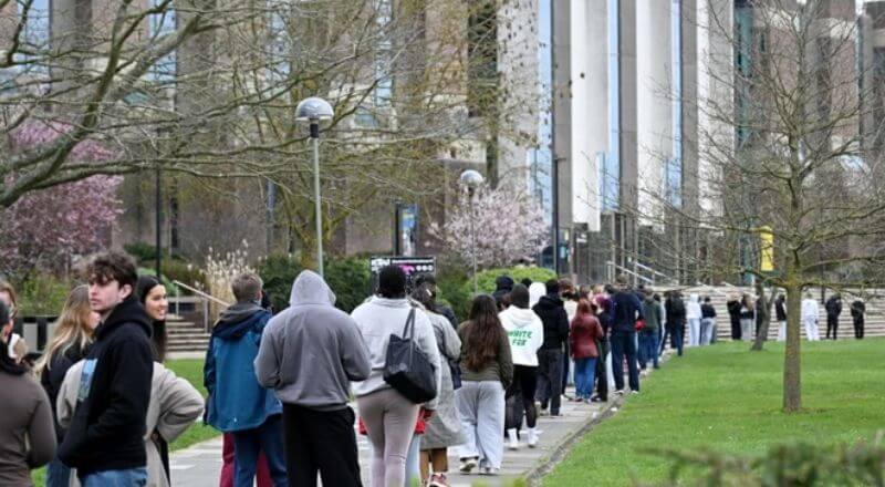 Hàng dài sinh viên tụ tập trước một tòa nhà tại Đại học Kent, Canterbury, để nhận thuốc kháng sinh