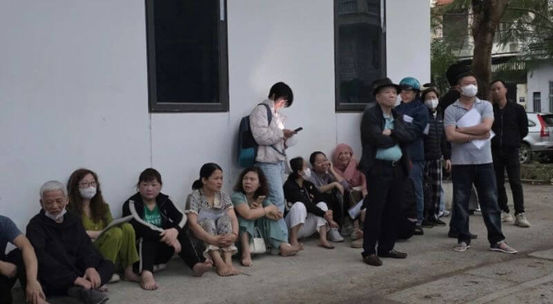 Phụ huynh đang trú mưa trong lúc xếp hàng đợi mua hồ sơ